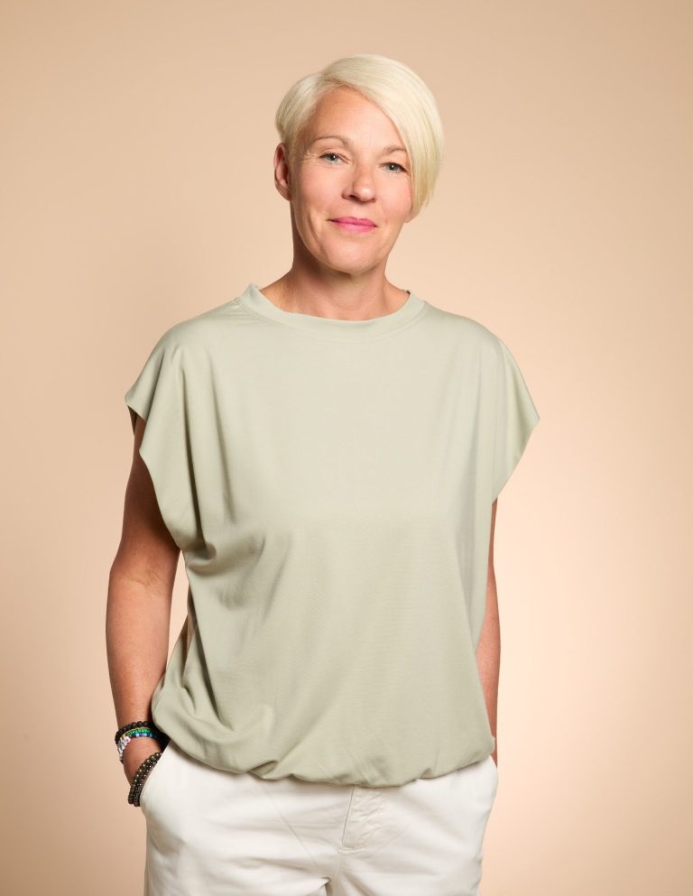 Nadja Hummer lädt Sie ein zum Gespräch. Nadja Hummer schaut in die Kamera und lächelt sie auffordernd an. Sie hat ein hellgrünes T-Shirt und eine weiße Hose an. Der Blick ist offen